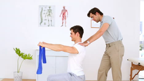 Physiotherapist-checking-shoulders-of-patient-pulling-resistance-band