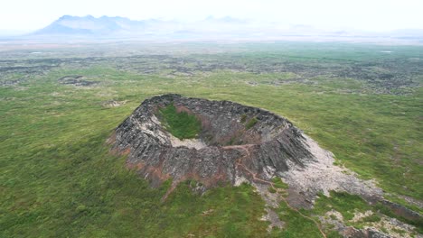 aerial volcano eldborg, push out movement, green summer hazy misty volcanic landscape, shrub spatter cone, touristic trail for outdoor travellers