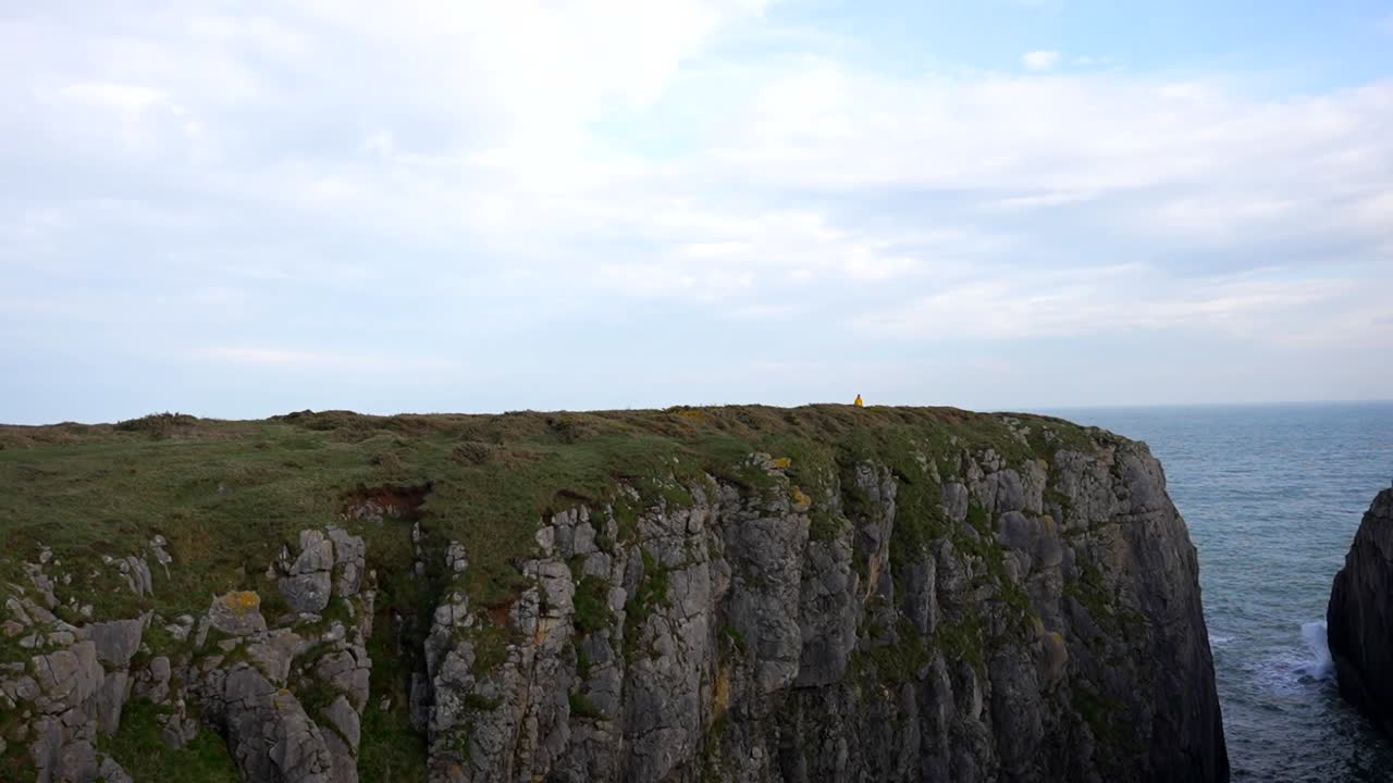 человек в желтом плаще идет рядом с скалой на расстоянии