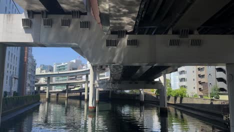 underneath a city bridge over a calm river, with buildings on a clear day, no people visible