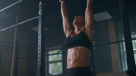 movimiento lento: levantar los pies hasta la barra en la barra del gimnasio mujer muscular atractiva ejercicio y entrenamiento en el gimnasio. atleta femenina de pie en una barra horizontal levanta las piernas para entrenar los músculos de los abdominales