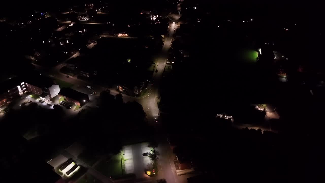 White car on illuminated street of american town. Night scene with lighting lantern along road. Houses and homes in small town of USA. Aerial Birds Eye tracking shot