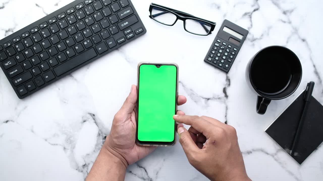 Person holding a smartphone with a green screen, surrounded by office supplies
