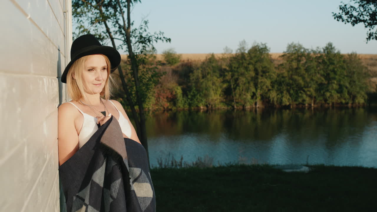 한 여자가 그림 같은 호수가 내려다보이는 집 벽에 기대어 서 있다