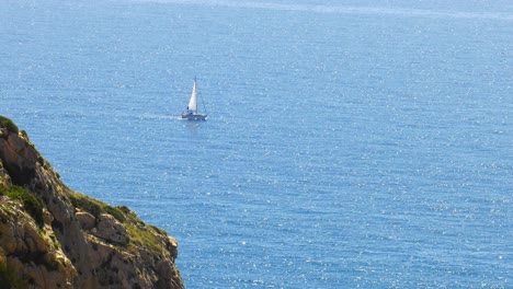 sailboat on wide blue ocean with sea cliffs in foreground, slow motion