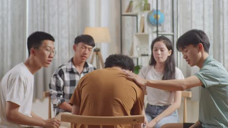 아시안 십대 그룹은 의자에 앉아서 집에서 토론하는 원을 형성합니다. 십대 학생들은 갈색 티셔츠를 입은 소년을 지지합니다.