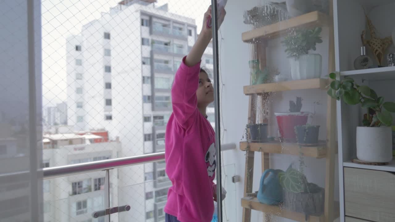 Giovane ragazza che pulisce una finestra di vetro sul balcone di un appartamento.