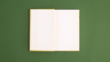 light green vintage hardcover book appear and open with copy space on dark green background. stop motion flat lay