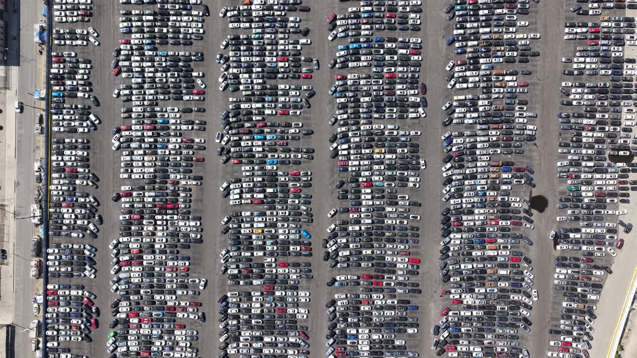 Metraje aéreo cinematográfico diurno, grabado con dron desde una perspectiva elevada a vista de pájaro en Los Ángeles, que muestra un lento movimiento de dolly hacia adelante sobre un denso desguace de coches urbano.