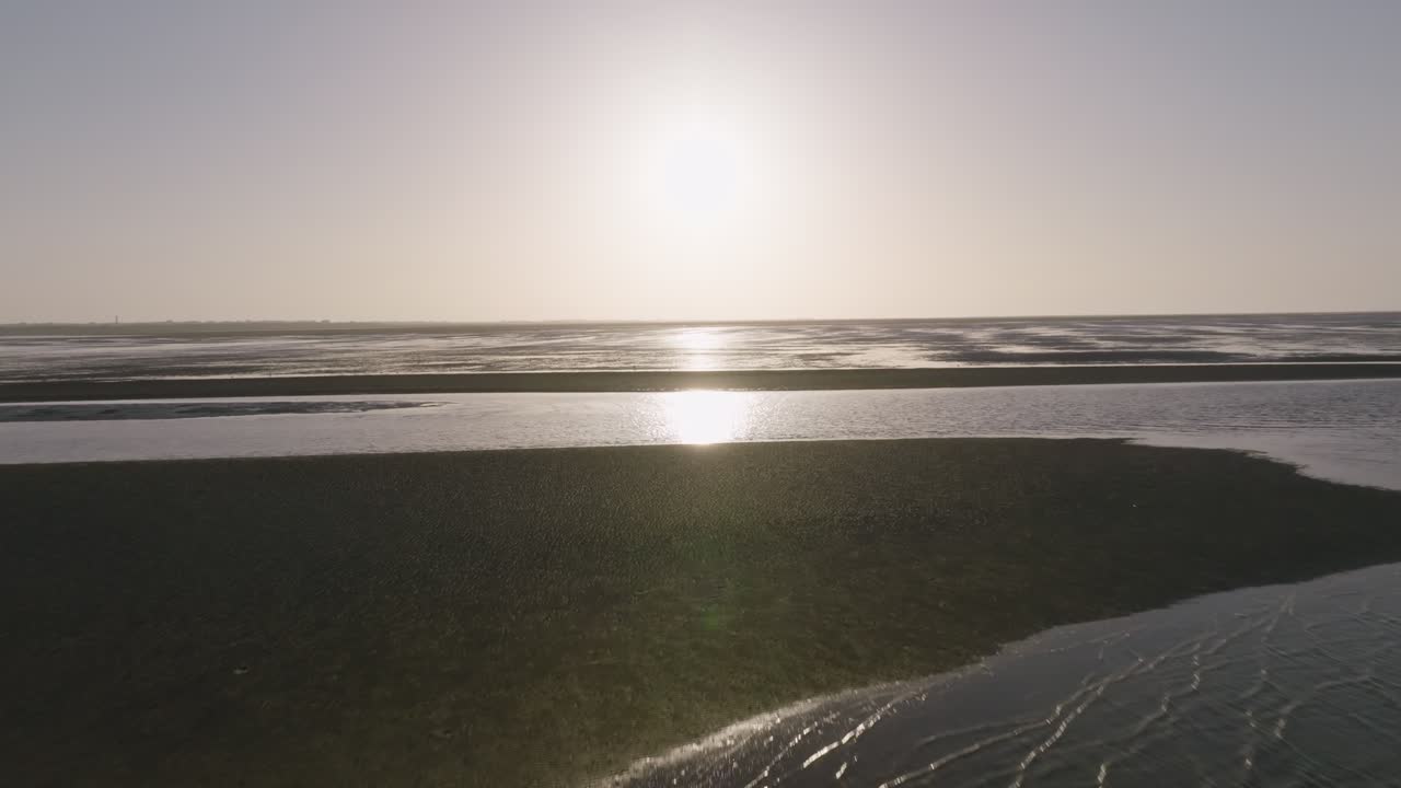 Bright morning flyover across open water towards wadden sea under clear sky