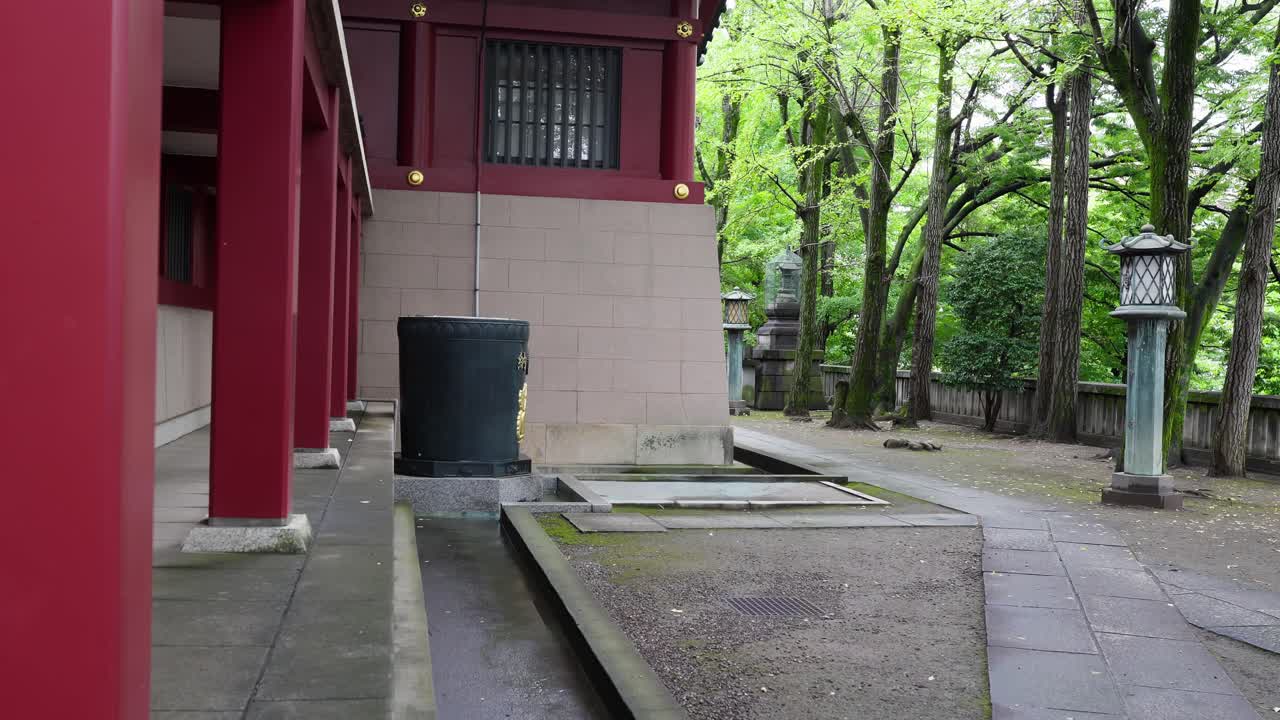 A peaceful scene showing a stone path leading past traditional red temple buildings and ornate lanterns in a serene outdoor setting