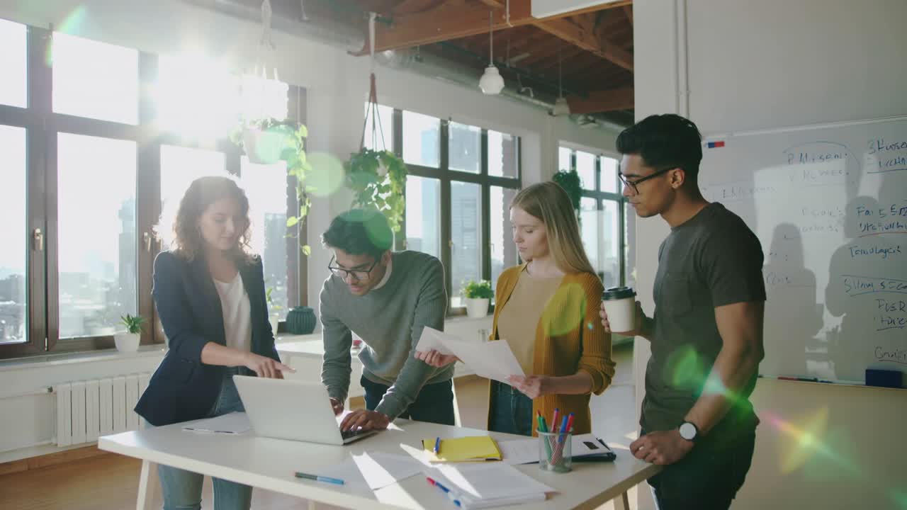 Pointing leader guiding typing peer on laptop in office business casual, working on project papers