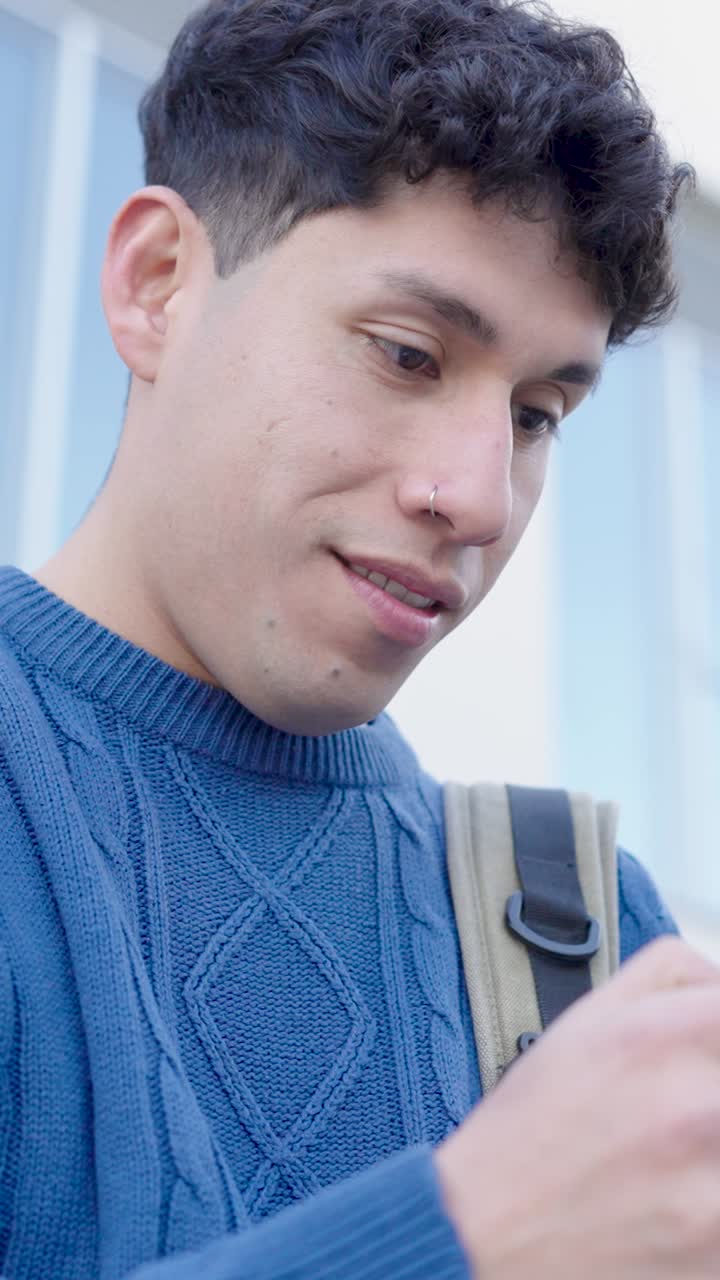 Young latin american student smiling and using smartphone. Vertical