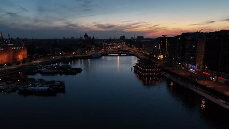aerial zoom out over a quiet marina in amsterdam during blue hour, revealing the city skyline and canal lights