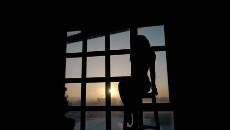 silhouette of emotional slim woman on bar stool in dark room