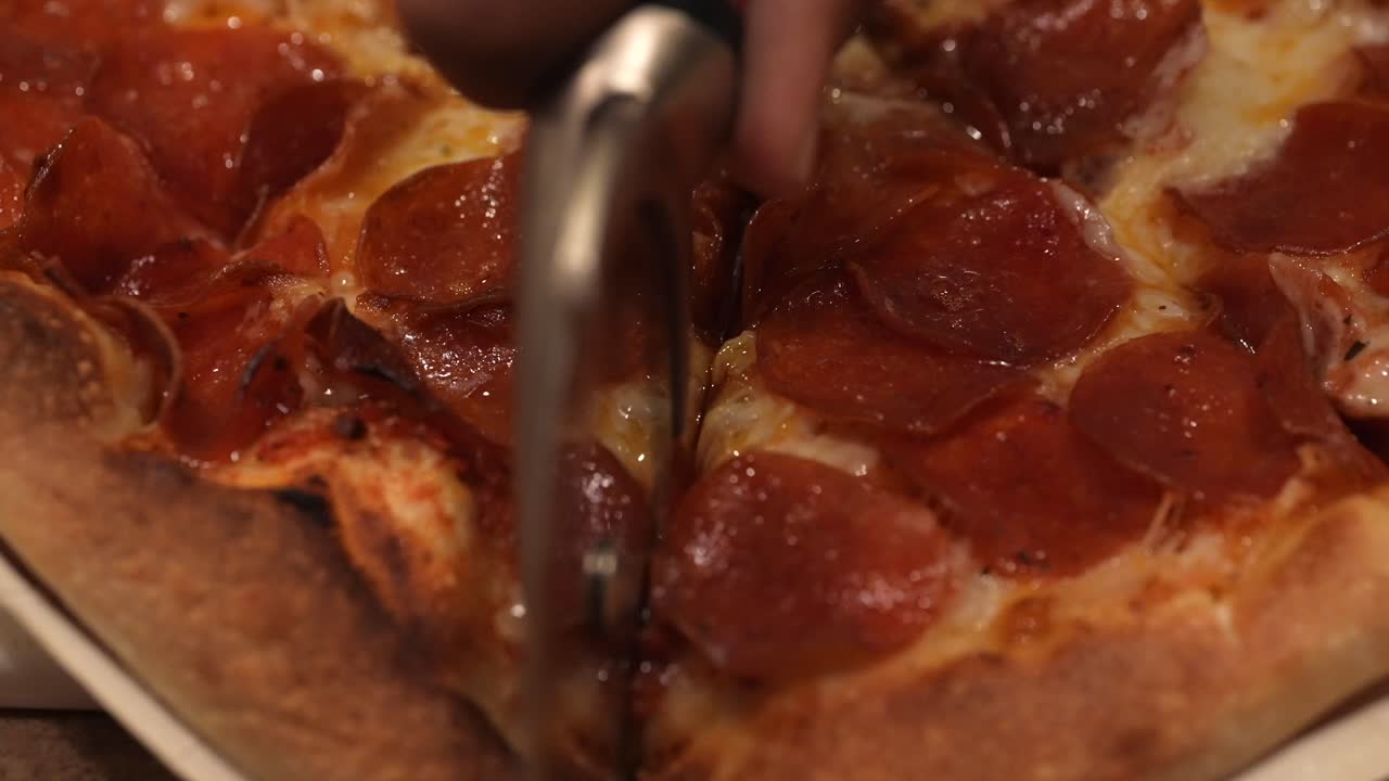 usando una rueda de pizza para cortar una pizza de pepperoni casera recién horneada en porciones - cierre aislado