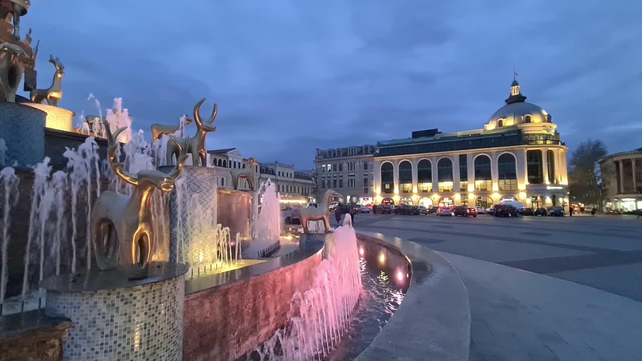 Evening view of a city square with a fountain and statues