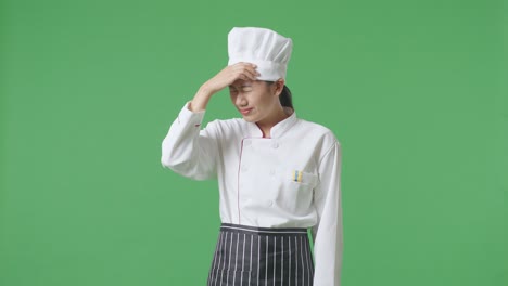 asian woman chef having a headache while standing in the green screen background studio