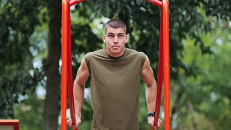 joven deportista atlético haciendo pull-ups en la instalación deportiva roja en el parque