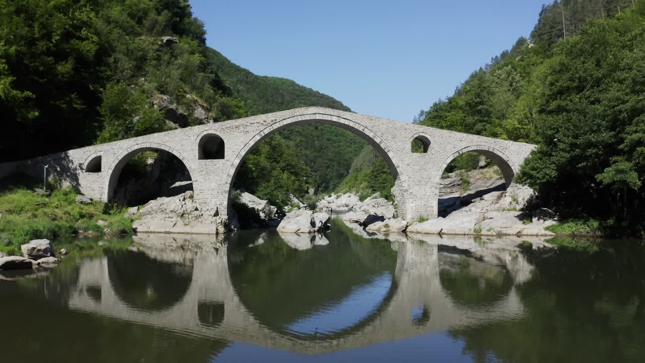 Approaching drone shot going under the main arch of the Devil's Bridge located in Ardino at the foot of Rhodope Mountain in Bulgaria