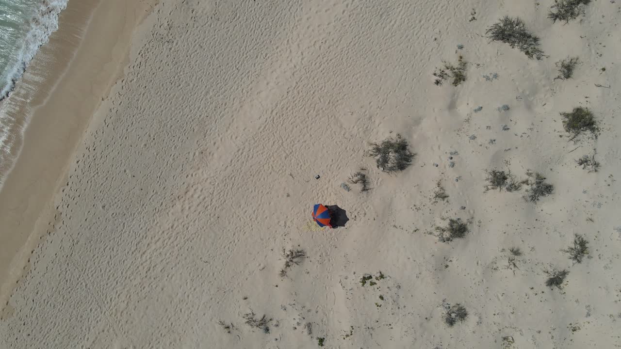 AEREA - Persona sotto un parasole nella soleggiata Exmouth, Australia, ripresa in discesa dall'alto.