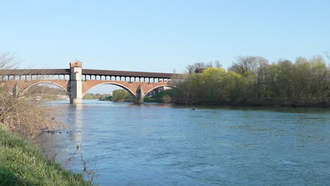 폰테 코페르토 (ponte coperto) 는 파비아의 티치노 강 (ticino river) 을 가로지르는 다리로, 은 날, 카누를 타고 항해하는 사람, 롬바르디아, 파비아, 이탈리아.