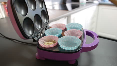 adding cake mixture to paper baking tray with a spoon in a cupcake maker