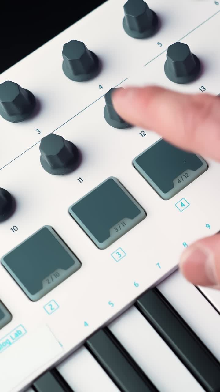 Close-up of a hand turning a knob on a MIDI keyboard controller with drum pads, adjusting sound settings in a home studio, shallow depth of field, vertical