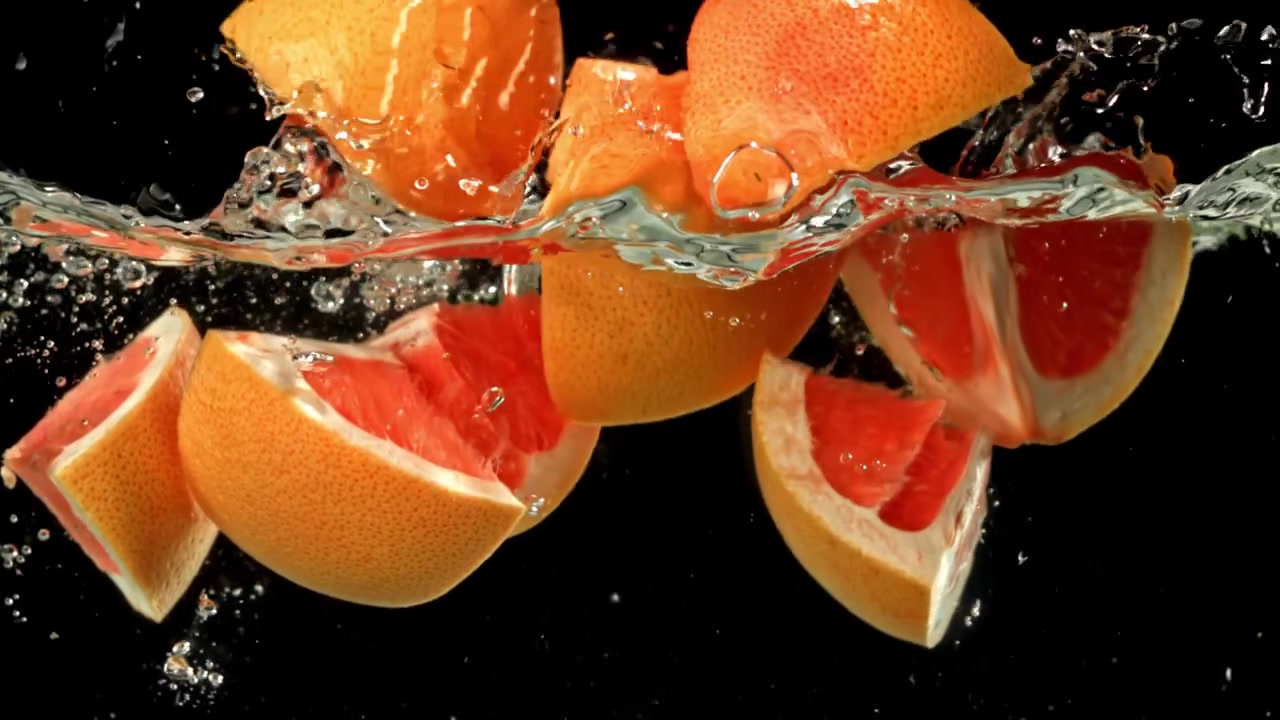Grapefruktskiver faller ned i vann i sakte film