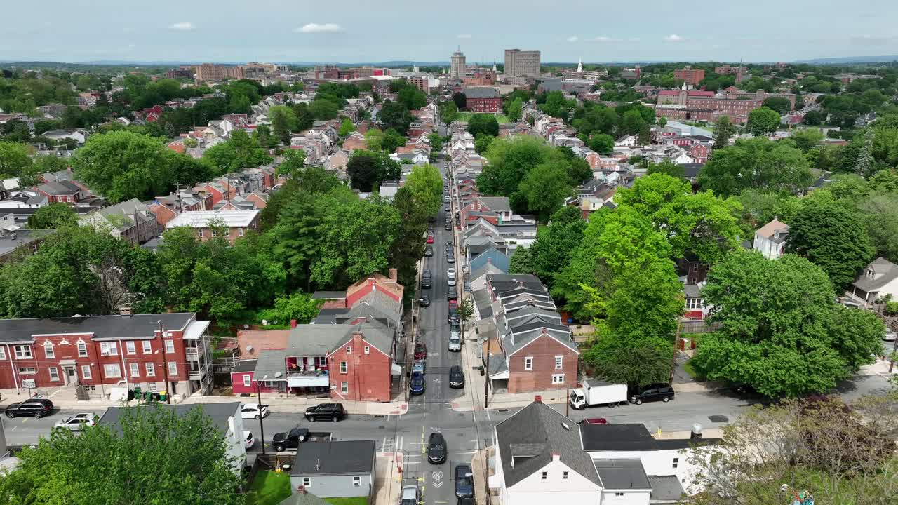 Junction with cars on american suburb town with green trees. Descend drone wide shot. Green trees and sunny day in American town. Downtown with towers in background.