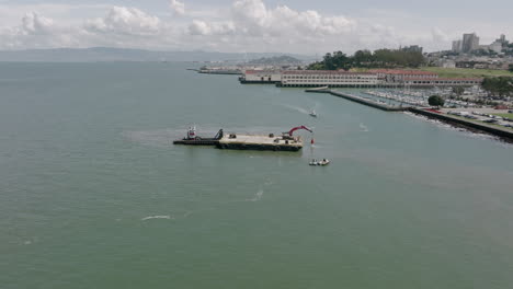 slow aerial pedestal shot of a barge pulling things out of the water in san francisco, california