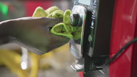 close-up of hand cleaning coffee machine display and button with green cloth, wiping smudges and ensuring cleanliness, showing focus on kitchen appliance care and maintenance