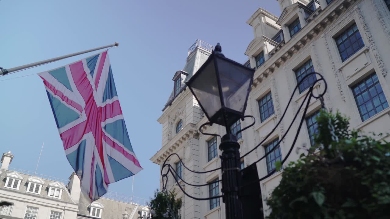 British flag is flapping near to a traditional street lamp on a clear blue sky around Victorian architecture buildings