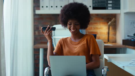 Joven-Empresaria-Sonriente-Trabajando-En-Un-Escritorio-En-La-Oficina-Hablando-Por-El-Micrófono-Del-Teléfono-Móvil