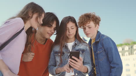 un grupo de adolescentes con dos chicas y dos chicos viendo algo en la pantalla de un teléfono móvil 3