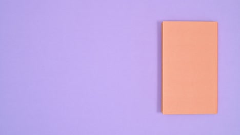 orange hardcover vintage book move from right to left side of purple theme and open. stop motion flat lay