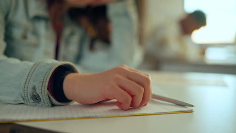 student writing on notebook with pen in classroom