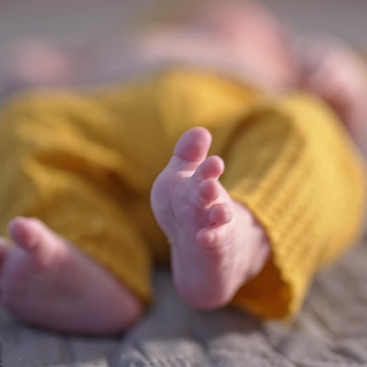 Lille barn i gule bukser ligger på sengen med sine små fødder mod kameraet. Smukke små babyfødder i nærbillede.