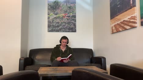 un hombre se sienta en un sofá con auriculares y lee y escribe en un libro