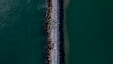 vista de pájaro del embarcadero del océano de la pared de roca creando un banco de arena, día soleado