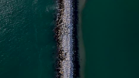 birdseye view of rock wall ocean jetty creating a sand bank, sunny day