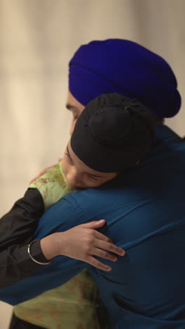 vertical video studio shot of loving sikh father embracing son both wearing turbans against plain background