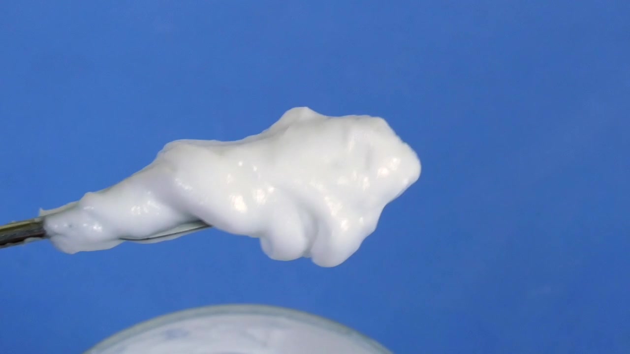 Crema cosmetica bianca, gel o lozione mescolata con una spatola in un laboratorio scientifico.