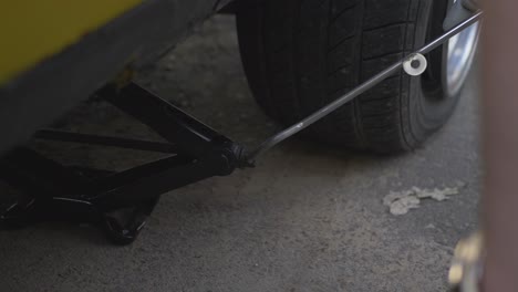 a man with a lifting jack lifts a yellow car with a flat tire-1