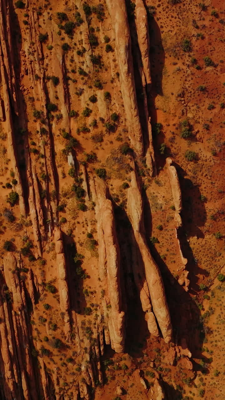 Car going by the road parallel to the oddly-shaped mountains. Dry orange landscape of desert in Utah, USA from aerial view. Vertical video