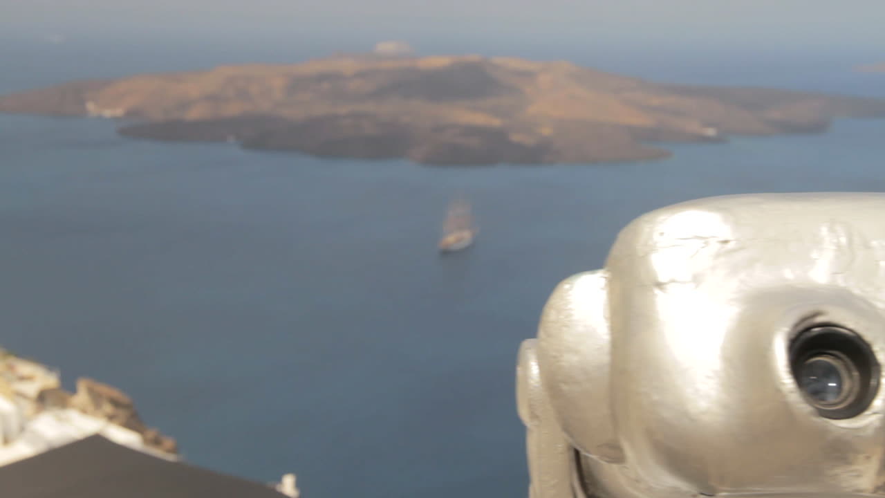 vista de la isla volcánica de nea kameni dentro de la caldera de santorini, mientras pasamos cerca de un par de binoculares públicos