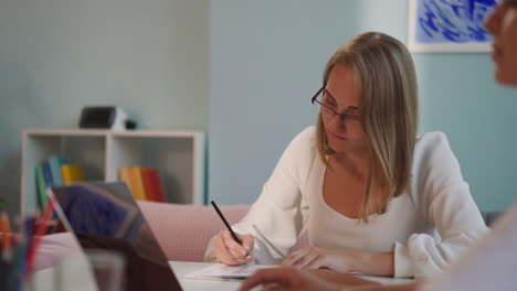 mujer rubia enfocada con gafas hace notas en el libro de ejercicios