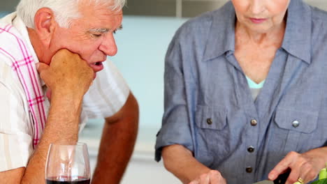 una pareja de ancianos preparando una comida saludable mientras beben vino rojo