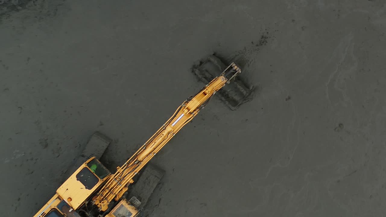 vista aérea de arriba hacia abajo de una excavadora que mueve lodo en un sitio de construcción