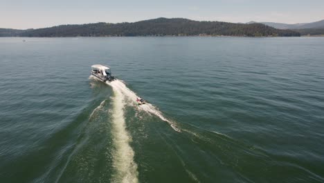 pontoon boat pulling two kids on a tube on a lake with mountains